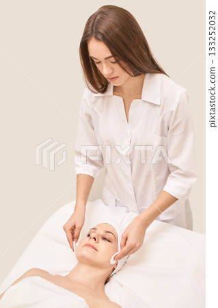 Young caucasian female therapist applying skincare treatment to relaxed adult 133252032