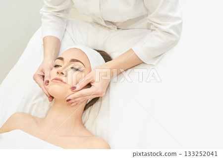 Young caucasian female receiving facial massage from therapist in spa setting 133252041