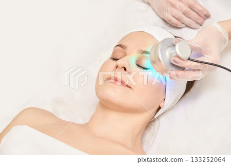 Caucasian female undergoing facial light therapy treatment in spa setting 133252064