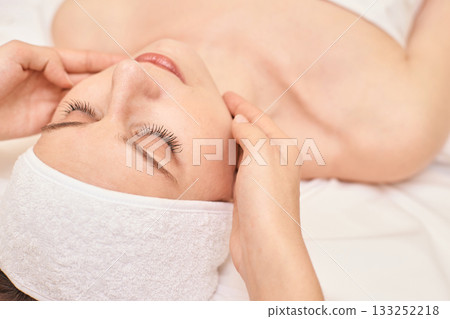 Caucasian female receiving relaxing facial massage in spa setting with calm 133252218