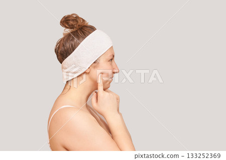 Caucasian adult female with headband examining skin profile in neutral Caucasian adult female with headband examining skin profile in neutral 133252369