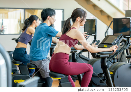 Men and women using upright bikes at the gym 133253705