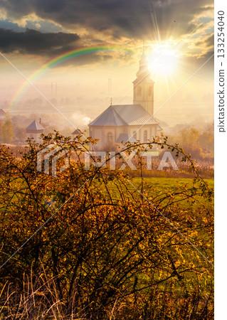 old church in the village in autumn at sunset. view of countryside landscape from a hill in hazy evening light. empty rural fields. pilgrimage storytelling image under the rainbow 133254040