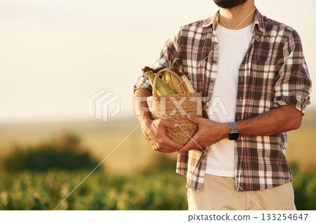 Holding the corn in paper package. Farmer is on the agricultural field Holding the corn in paper package. Farmer is on the agricultural field 133254647