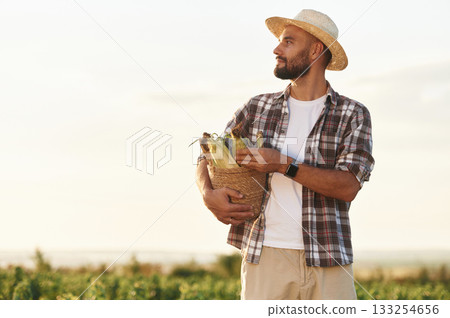 Paper package with corn in hands. Farmer is on the agricultural field Paper package with corn in hands. Farmer is on the agricultural field 133254656