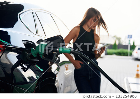 Smartphone in hands. A young woman at a gas station with her car Smartphone in hands. A young woman at a gas station with her car 133254906