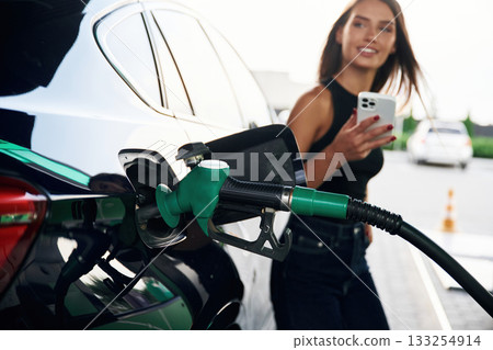 Waiting, holding smartphone. A young woman at a gas station with her car 133254914