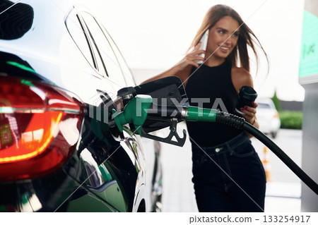 Talking by a phone. A young woman at a gas station with her car Talking by a phone. A young woman at a gas station with her car 133254917