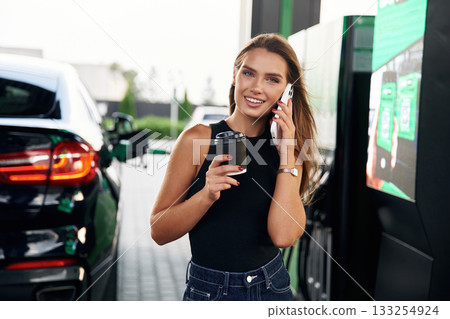 Having a conversation by phone. A young woman at a gas station with her car 133254924