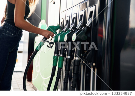Pump nozzle in the hand. A young woman at a gas station with her car 133254957