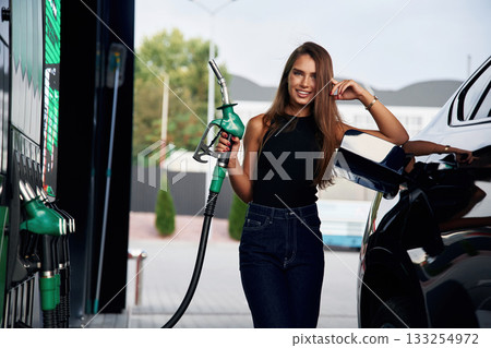 Pump nozzle in the hand. A young woman at a gas station with her car Pump nozzle in the hand. A young woman at a gas station with her car 133254972