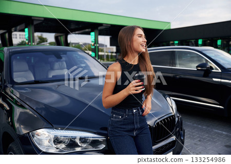 Front view, standing. A young woman at a gas station with her car Front view, standing. A young woman at a gas station with her car 133254986