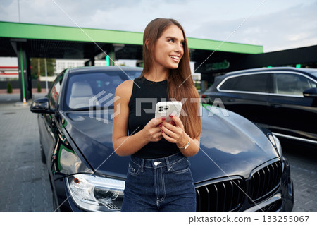White smartphone in hands. Woman is near her car outdoors 133255067