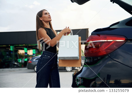 Trunk is opened. Woman is near her car outdoors 133255079