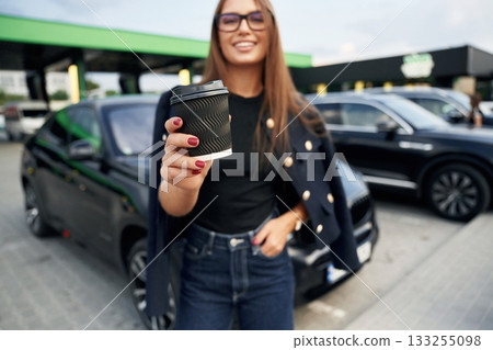Happy owner with cup of drink. A young woman at a gas station with her car Happy owner with cup of drink. A young woman at a gas station with her car 133255098