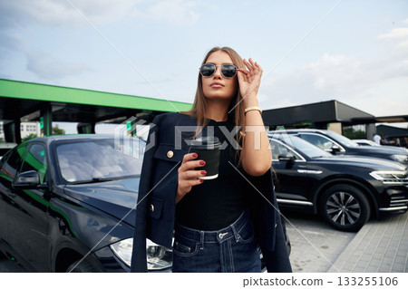 In sunglasses. A young woman at a gas station with her car In sunglasses. A young woman at a gas station with her car 133255106
