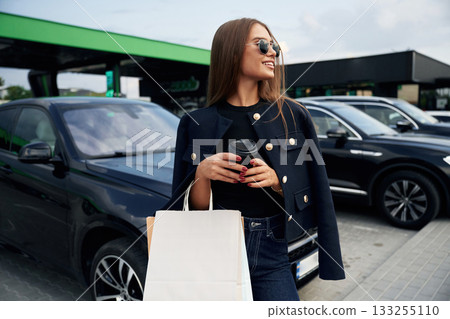 Shopping bags in hand. A young woman at a gas station with her car Shopping bags in hand. A young woman at a gas station with her car 133255110