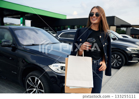 Shopping bags in hand. A young woman at a gas station with her car Shopping bags in hand. A young woman at a gas station with her car 133255111