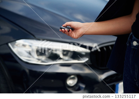Focused close up view of woman hand that is holding key in front of the car 133255117
