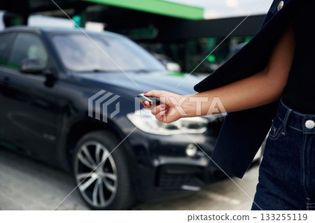 Focused close up view of woman hand that is holding key in front of the car 133255119