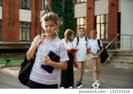 Portrait of girl that is standing in front of her friends. Kids are near the school together, pupils Portrait of girl that is standing in front of her friends. Kids are near the school together, pupils 133255426