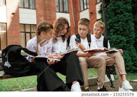 Sitting on the bench. Kids are near the school together, pupils Sitting on the bench. Kids are near the school together, pupils 133255579