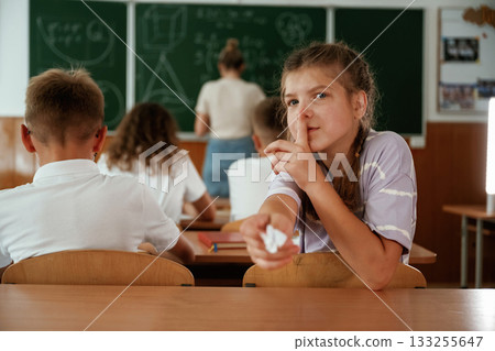 Girl is gives a cheat sheet. Pupils, kids in the classroom together 133255647