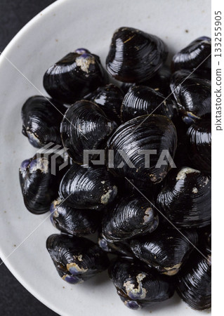 Large Yamato Shijimi clams on a plate against a black background 133255905