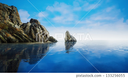 Crystal clear waters gently lap against rugged rocks under a brilliant blue sky, creating a serene landscape perfect for relaxation and contemplation by the ocean. 133256055