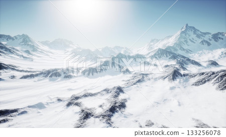 Majestic mountains rise sharply against the backdrop of a clear blue sky. Bright sunlight illuminates the snow covered peaks, creating a serene and breathtaking winter scene. 133256078