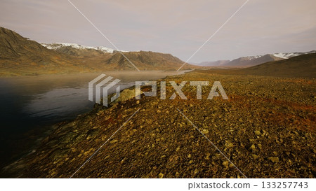 A peaceful scene unfolds along a rocky shoreline as the sun rises over distant mountains. Mist drifts above the calm river, illuminating the landscape with soft colors. A peaceful scene unfolds along a rocky shoreline as the sun rises over distant mountains. Mist drifts above the calm river, illuminating the landscape with soft colors. 133257743