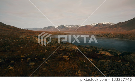 Expansive view of a serene river flowing through a valley surrounded by majestic mountains. The sky glows softly as dusk settles, casting stunning colors over the landscape. 133257746