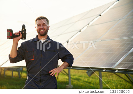 Ready for the work. With drill. Man is near solar panels outdoors at daytime 133258095