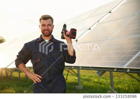 Ready for the work. With drill. Man is near solar panels outdoors at daytime 133258096