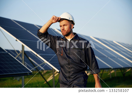 Touching the white hard hat. Man is working with solar panels outdoors at daytime Touching the white hard hat. Man is working with solar panels outdoors at daytime 133258107