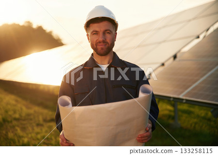Paper plan in hands. Man is working with solar panels outdoors at daytime Paper plan in hands. Man is working with solar panels outdoors at daytime 133258115