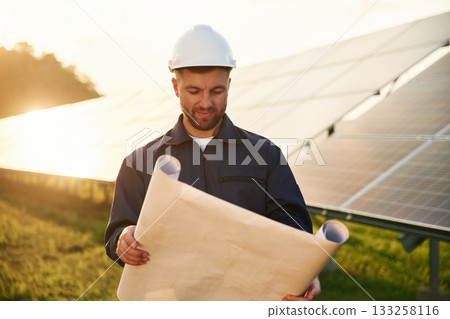 Paper plan in hands. Man is working with solar panels outdoors at daytime 133258116