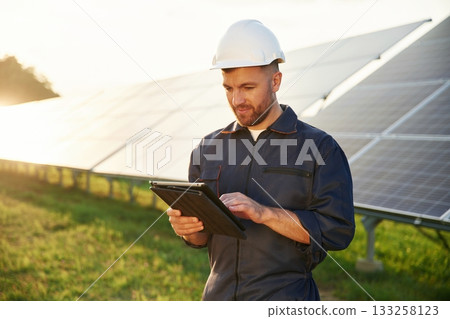 Reflection of the sunlight behind. Man is working with solar panels outdoors at daytime Reflection of the sunlight behind. Man is working with solar panels outdoors at daytime 133258123