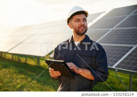 Digital tablet in hands. Man is working with solar panels outdoors at daytime Digital tablet in hands. Man is working with solar panels outdoors at daytime 133258124