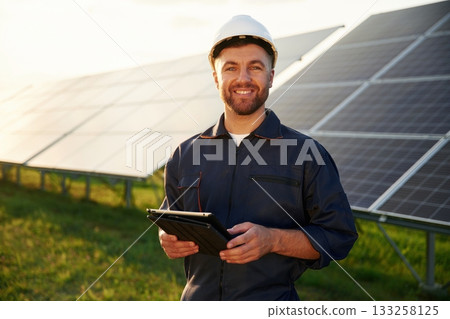 Digital tablet in hands. Man is working with solar panels outdoors at daytime Digital tablet in hands. Man is working with solar panels outdoors at daytime 133258125