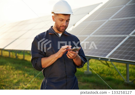 Phone in hands, internet connection. Man is working with solar panels outdoors at daytime Phone in hands, internet connection. Man is working with solar panels outdoors at daytime 133258127
