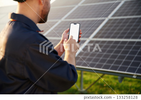Phone in hands, internet connection. Man is working with solar panels outdoors at daytime Phone in hands, internet connection. Man is working with solar panels outdoors at daytime 133258128