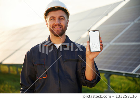 Smartphone with copy space on it. Man is working with solar panels outdoors at daytime Smartphone with copy space on it. Man is working with solar panels outdoors at daytime 133258130
