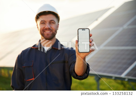 Smartphone with copy space on it. Man is working with solar panels outdoors at daytime 133258132