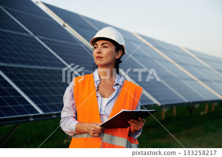 Checking the data, with notepad. Female worker engineer in uniform is near solar panels Checking the data, with notepad. Female worker engineer in uniform is near solar panels 133258217