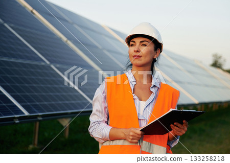 Checking the data, with notepad. Female worker engineer in uniform is near solar panels Checking the data, with notepad. Female worker engineer in uniform is near solar panels 133258218