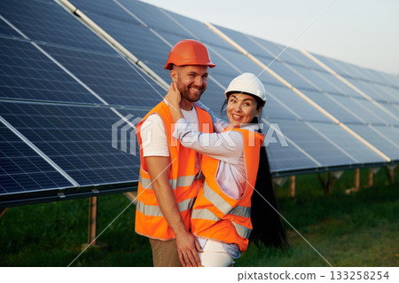 Playful mood, embracing each other. Man and woman, workers are near solar panels, in uniform Playful mood, embracing each other. Man and woman, workers are near solar panels, in uniform 133258254