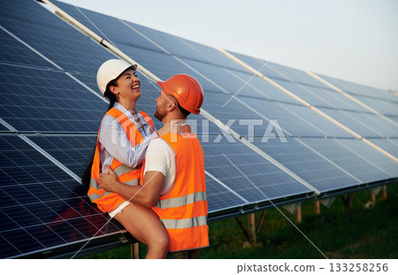 Playful mood, embracing each other. Man and woman, workers are near solar panels, in uniform 133258256