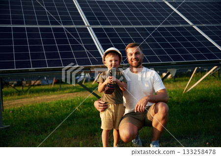 Posing with drill in hands. Father with his little son are together near the solar panels Posing with drill in hands. Father with his little son are together near the solar panels 133258478