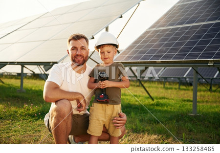 In hard hat and with drill. Father with his little son are together near the solar panels 133258485